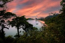 Вражаючий вид океану з човном проти буйних зелених дерев під небом з пухнастими хмарами на заході сонця в Таїланді. — стокове фото