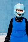 Reife Frau in Sportbekleidung und Boxhandschuhen steht mit Helm vor blauer Wand und blickt in die Kamera — Stockfoto