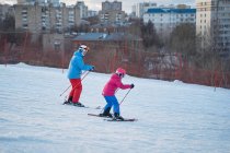 Side view parent in warm sportswear and helmet teaching little kid to ski alongside snowy hill slope in winter ski resort — Stock Photo