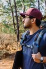 Bearded male backpacker in cap walking among trees and plants in woods in sunny day — Stock Photo