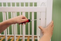 Crop woman with screwdriver leaning forward while mounting crib at home on sunny day — Stock Photo