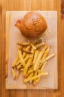 Вид сверху на вкусный свежий гамбургер и хрустящие французские фри, подаваемые на деревянной доске в современном ресторане быстрого питания — стоковое фото