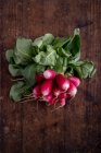 Top view of heap of raw radish with curved leaves and roots on brown background — Stock Photo