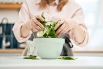 Неузнаваемая женщина с листьями шпината на столе во время приготовления пищи в доме — стоковое фото