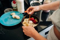 From above crop unrecognizable person topping tasty healthy porridge with banana and strawberries in kitchen — Foto stock