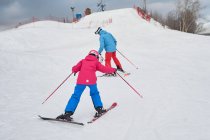 Ganzkörpergesichtsloser Elternteil in warmer Sportbekleidung und Helm bringt kleinem Kind das Skifahren am schneebedeckten Hang im Winterskigebiet bei — Stockfoto