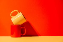 Creative colorful mugs on yellow and red background in studio — Stock Photo