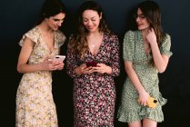 Contenidos jóvenes mejores amigas en ropa de moda con teléfonos celulares de pie en la pasarela urbana contra la pared - foto de stock