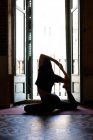 Vue latérale d'une femme mince assise sur un tapis à Eka Pada Rajakapotasana et pratiquant le yoga à la maison — Photo de stock