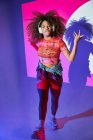Ganzkörpergefühllose Afroamerikanerin in kurzen Hosen, die über Kopfhörer Lieblingsmusik hört und im Studio in Neonlichter in die Kamera tanzt — Stockfoto
