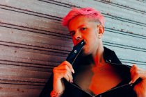 Молодой гомосексуалист с татуировкой и розовыми волосами в стильной верхней одежде смотрит в камеру на выветренную стену — стоковое фото