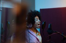 Cantante femenina negra interpretando canción contra micrófono con filtro pop mientras está de pie y mirando hacia adelante en el estudio de sonido - foto de stock