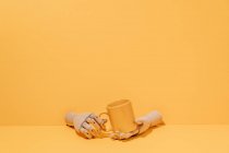 Творча декоративна дерев'яна рука тримає барвистий кухоль на жовтому фоні в студії — стокове фото