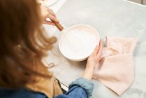 Contenido hembra joven en delantal batiendo crema dulce mientras se cocina en la mesa en casa de luz - foto de stock