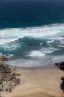 Dall'alto vista posteriore di viaggiatore femminile anonimo che ammira l'oceano schiumoso da spiaggia sabbiosa tra montagne — Foto stock
