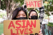 Етнічні жінки в масках тримають плакати, що протестують проти расизму на міській вулиці і дивляться геть — стокове фото