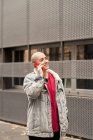 Persona transgénero en ropa casual hablando por teléfono celular mientras mira hacia otro lado contra el edificio urbano a la luz del día - foto de stock