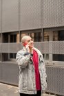 Transgender person in casual apparel talking on cellphone while looking away against urban building in daylight — Stock Photo