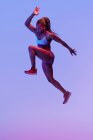 Вид сбоку решительной афроамериканки, прыгающей с летящими волосами, глядя вперед во время кардиотренировки — стоковое фото