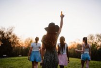 Back view of company of anonymous girlfriends with beer enjoying summer weekend at sunset in park — Stock Photo