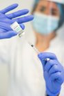 Ärztin mit Latex-Handschuhen und Gesichtsschutz füllt Spritze aus Flasche mit Impfstoff, um Patientin in Klinik während Coronavirus-Ausbruch zu impfen — Stockfoto