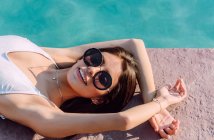 Junge weibliche Reisende in weißer Badebekleidung und moderner Sonnenbrille liegen an sonnigen Tagen am Pool — Stockfoto