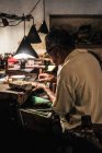 Seitenansicht eines reifen ethnischen Mannes, der am verwitterten Schreibtisch in der Handwerkswerkstatt arbeitet — Stockfoto