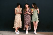 Зміст молодих кращих жінок-друзів у модному одязі з мобільними телефонами, що стоять на міській прогулянці на стіні — стокове фото