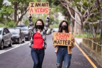 Mulheres étnicas em máscaras segurando cartazes protestando contra o racismo na rua da cidade e olhando para a câmera — Fotografia de Stock
