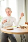 Heureuse astrologue féminine buvant une boisson chaude dans une tasse tout en regardant vers le bas à la maison au soleil — Photo de stock