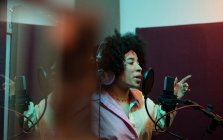 Чорна співачка виконує пісню проти мікрофона з поп-фільтром, стоячи і з нетерпінням чекаючи на звукову студію — стокове фото