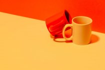 Creative colorful mugs on yellow and red background in studio — Stock Photo