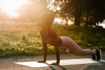 Vista lateral do ajuste atleta afro-americano feminino balanceamento na posição prancha enquanto faz exercícios abdominais no parque ao pôr do sol — Fotografia de Stock