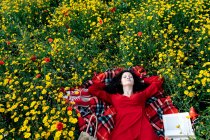From above of female with eyes closed having a break from reading textbook on blanket with handbag among blossoming daisies during a spring summer day — Stock Photo