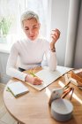 From above female astrologist taking notes in notepad at desk with cup of coffee at home in sunlight — Stock Photo