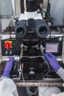 Обрізана невпізнавана людина-експерт в рукавичках лабораторного пальто, яка вивчає зразки за допомогою потужних лінз мікроскопа під час роботи в сучасній лабораторії — стокове фото