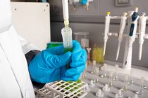 Químico anónimo de cultivo vertiendo aceite de marihuana de pipeta en tubo de muestra durante el examen en laboratorio - foto de stock