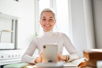 Smiling female blogger talking about astrology while recording video on cellphone at desk in sunlight — Stock Photo