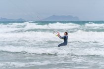 Активная спортсменка на кайтборде держит планку управления, практикуя кайтсерфинг и глядя вдаль на пенный океан — стоковое фото