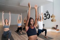 Vue latérale de la femme afro-américaine en compagnie de diverses personnes pratiquant le yoga à Warrior pose en studio — Photo de stock