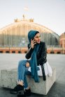 Muslim female in headscarf sitting on bench while talking mobile phone in city — Stock Photo