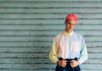 Autoconfianza joven gay en ropa de moda con el pelo rosa y tatuajes mirando a la cámara - foto de stock