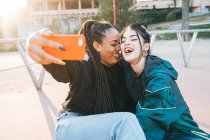 Молодая гомосексуальная женщина делает автопортрет по мобильному телефону в городе в подсветке — стоковое фото