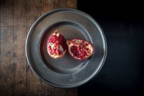 Vista aerea di deliziosi pezzi di melograno maturo con brillanti semi succosi sul piatto su sfondo marrone — Foto stock