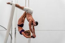 Volle Länge sportliche starke Frau, die auf dem Kopf stehend Split auf Antenne Seide und Anheben muskulösen männlichen Akrobat an den Händen während des Trainings zusammen im Fitness-Center — Stockfoto