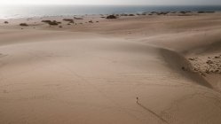 Сверху анонимная туристка в белом платье прогуливается по ребристому песку под легким небом — стоковое фото