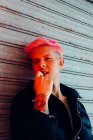 Young homosexual man with tattoo and pink hair in stylish outerwear looking at camera against weathered wall — Stock Photo