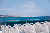 Chaises blanches vides sur le pont du bateau de croisière naviguant dans l'eau de mer bleue avec montagne sur le rivage — Photo de stock