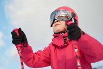 From below cute girl in pink warm activewear goggles and helmet skiing alongside snowy slope on clear winter day — Stock Photo