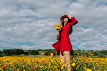 Da sotto di femmina elegante in cappello tra fiori fiorenti in campo di campagna durante giorno estivo — Foto stock
